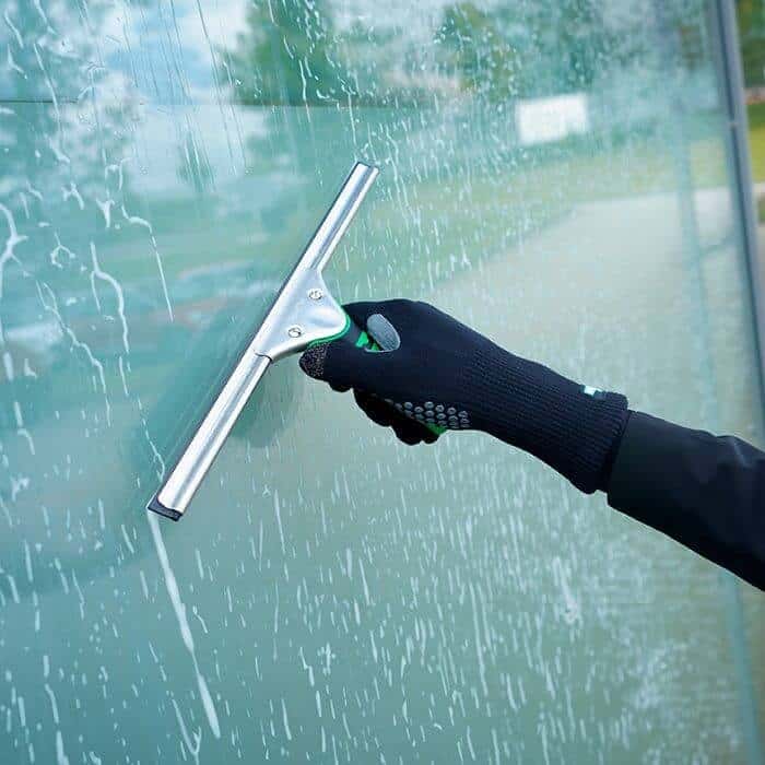 Professioneller Fensterabzieher von Unger Professioneller Unger-Fensterabzieher mit Gummiklinge, der mit einer behandschuhten Hand gehalten wird, für eine effiziente Glasreinigung in Gebäuden