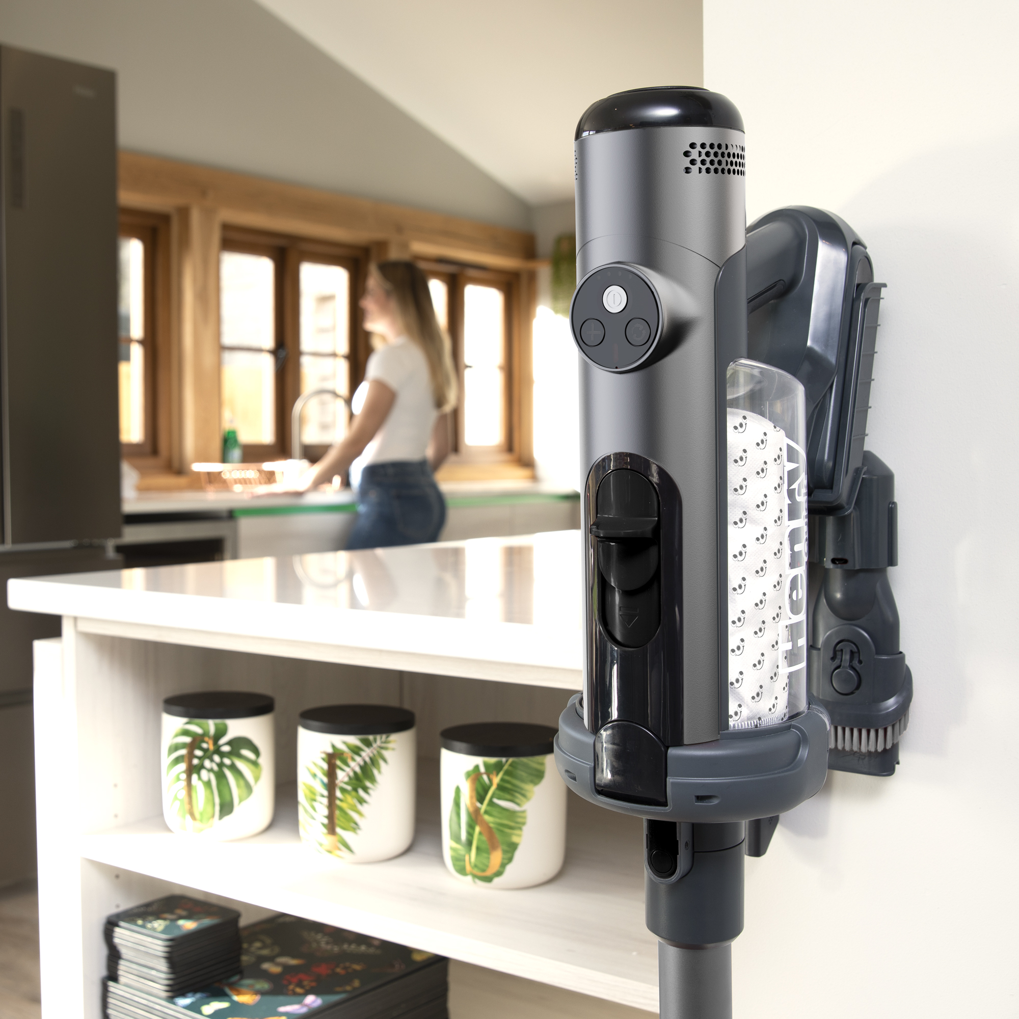 Henry Quick Akku-Staubsauger mit Wandhalterung und transparentem Staubbehälter, montiert an einer weißen Wand in einer Küche