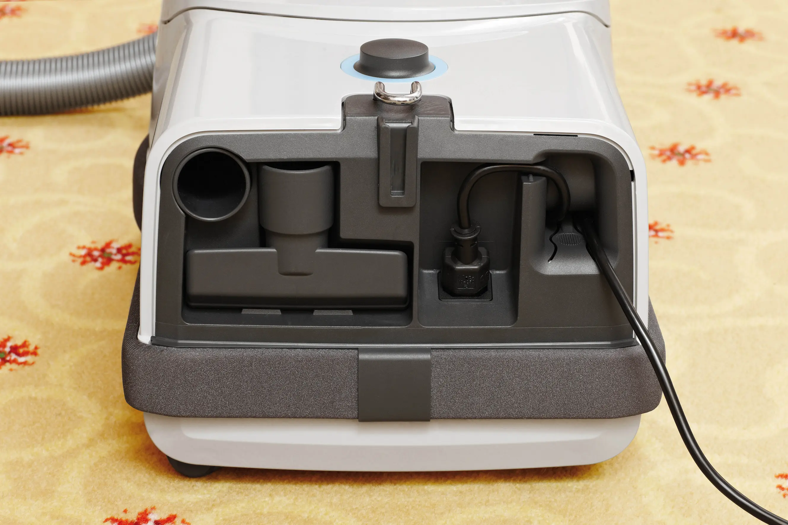 Rückansicht eines weiß-grauen Miele-Staubsaugers mit integriertem Netzkabel und verschiedenen Reinigungsaufsätzen zur Bodenreinigung.