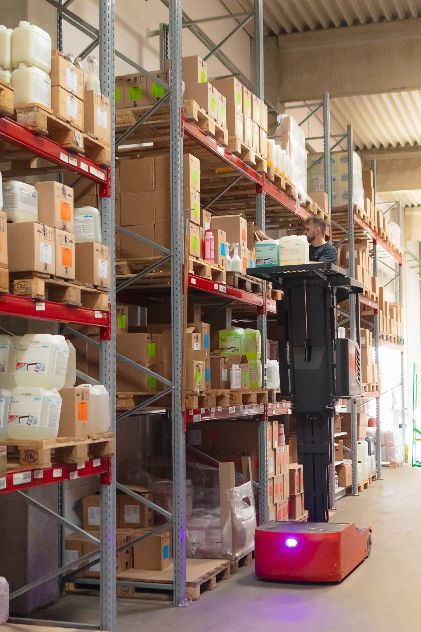 Mann auf Hubwagen im Lager mit Reinigungsmitteln in Flaschen und Kartons auf Regalen