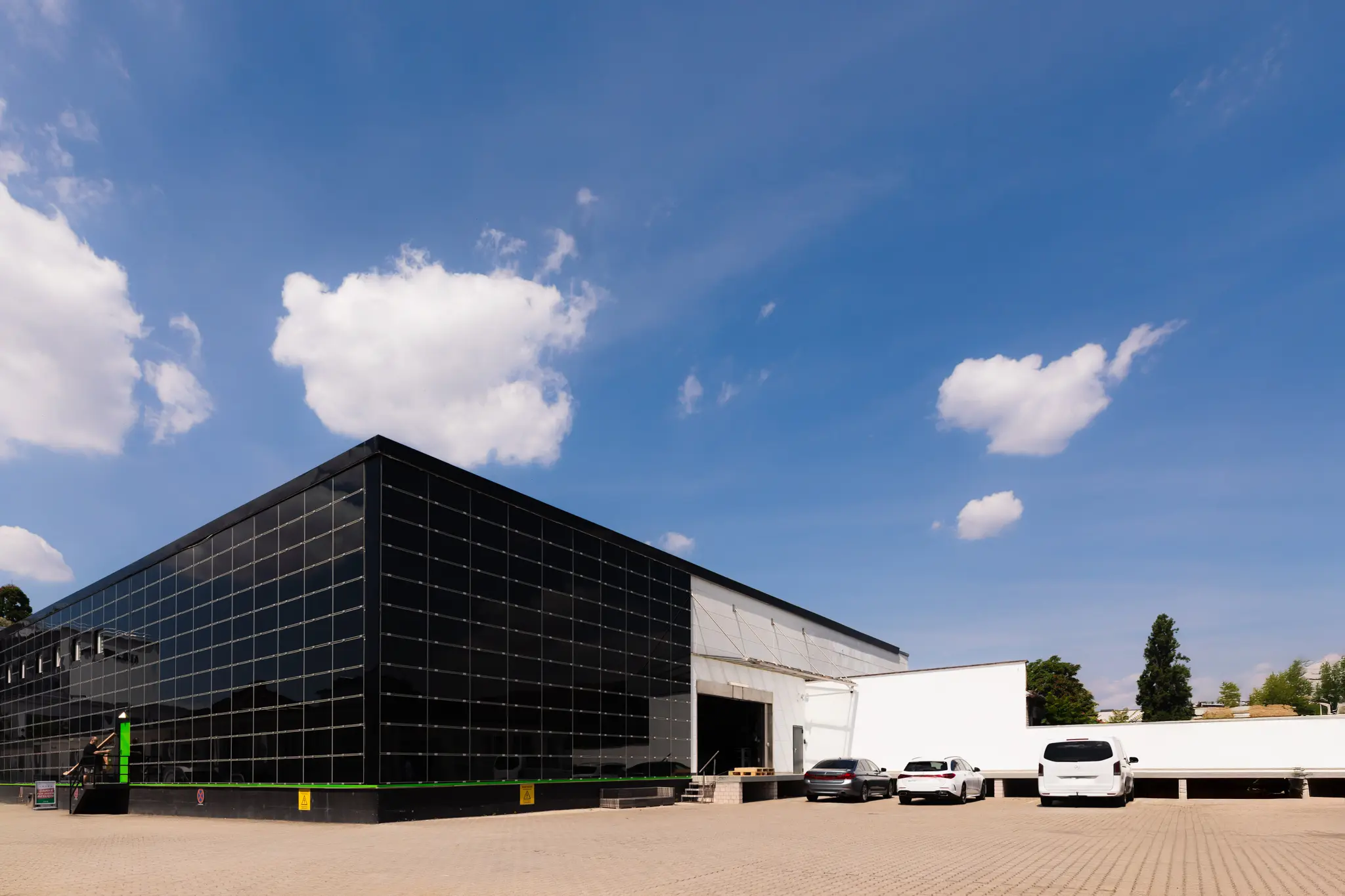 Moderne Lagerhalle mit schwarzer Glasfassade und weißen Lieferfahrzeugen auf dem Parkplatz
