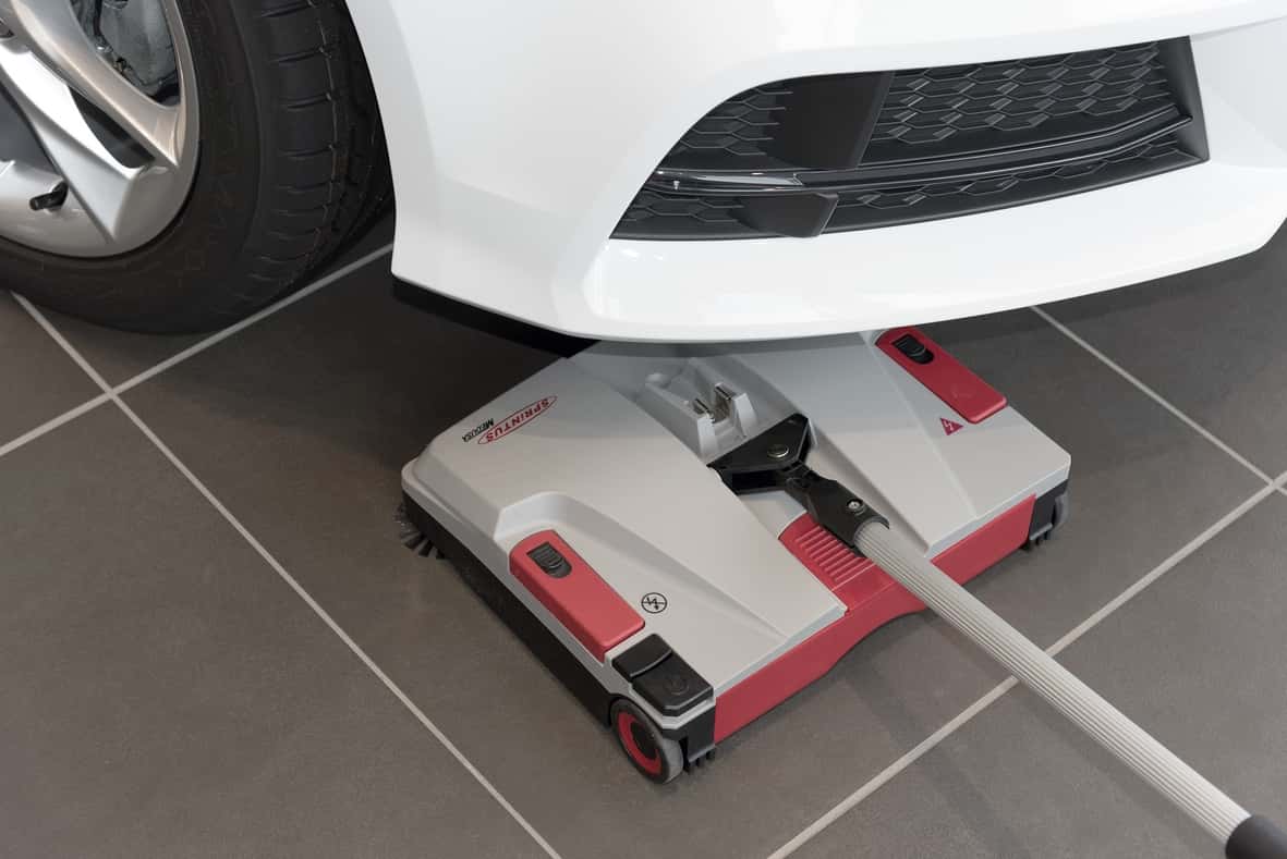Sprintus Kehrmaschine unter dem Auto Sprintus Kehrmaschine unter einem weißen Auto auf Fliesenboden.