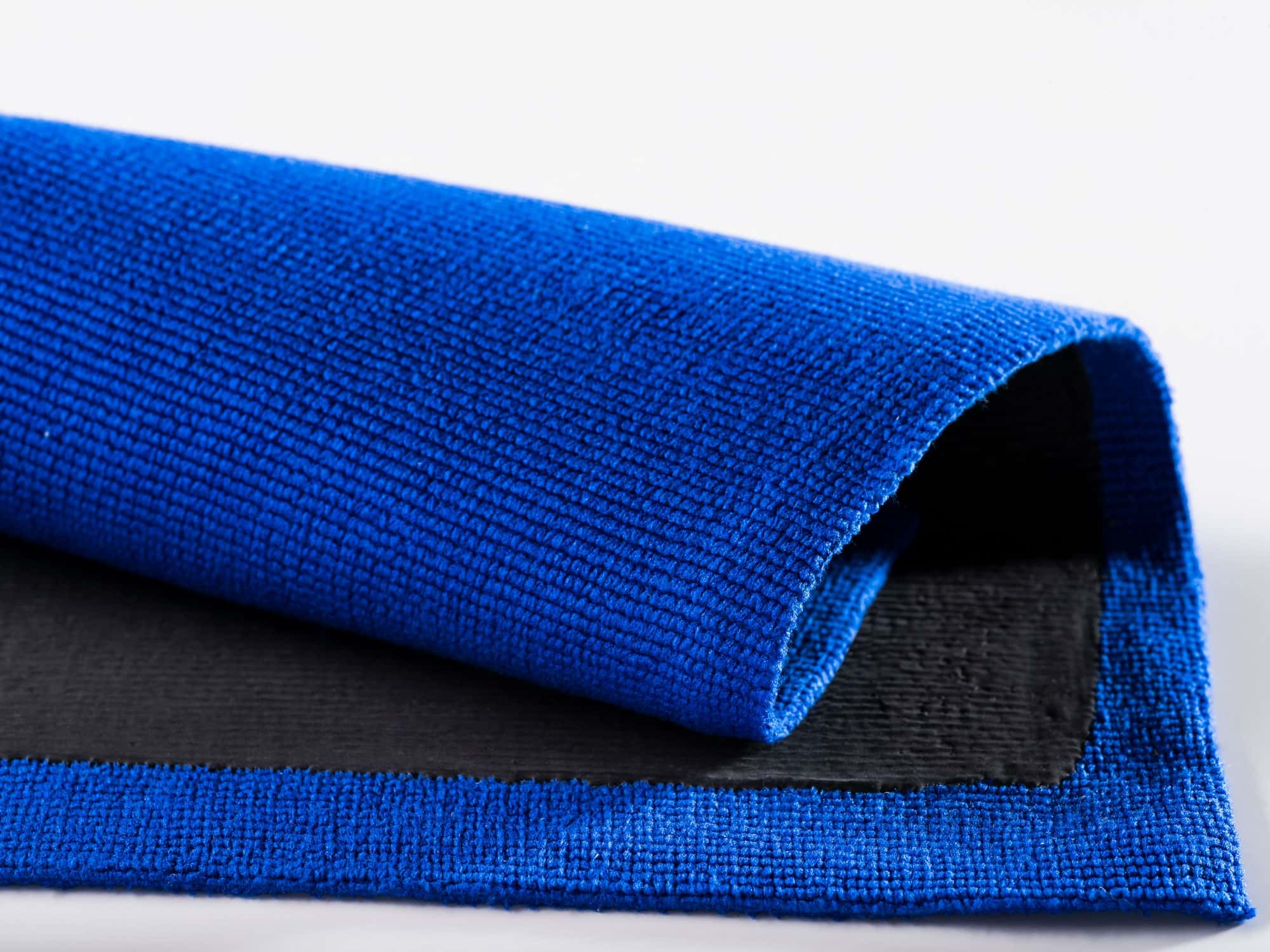 Blaues Mikrofasertuch mit schwarzer Unterseite, gerollt auf weißem Hintergrund für professionelle Reinigung