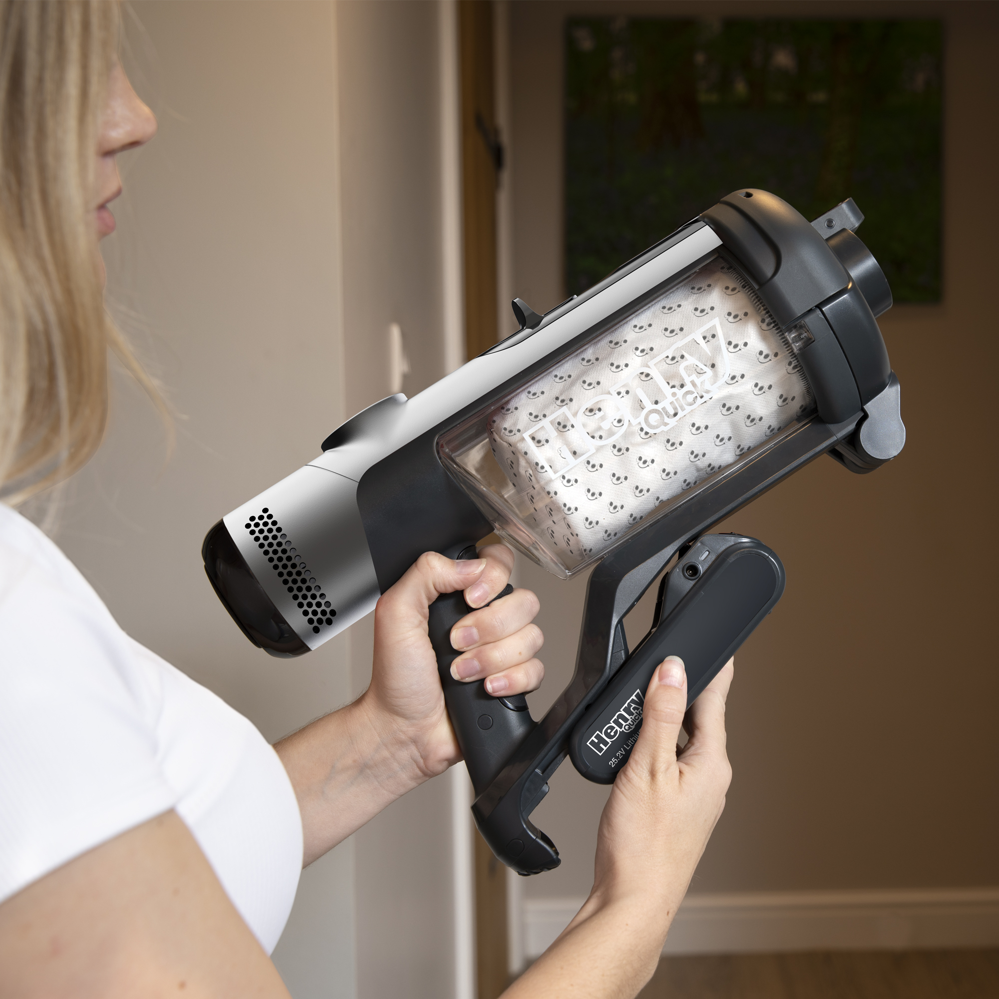 Henry Quick Akku-Staubsauger mit transparentem Staubbehälter und schwarzem Griff, gehalten von einer Person