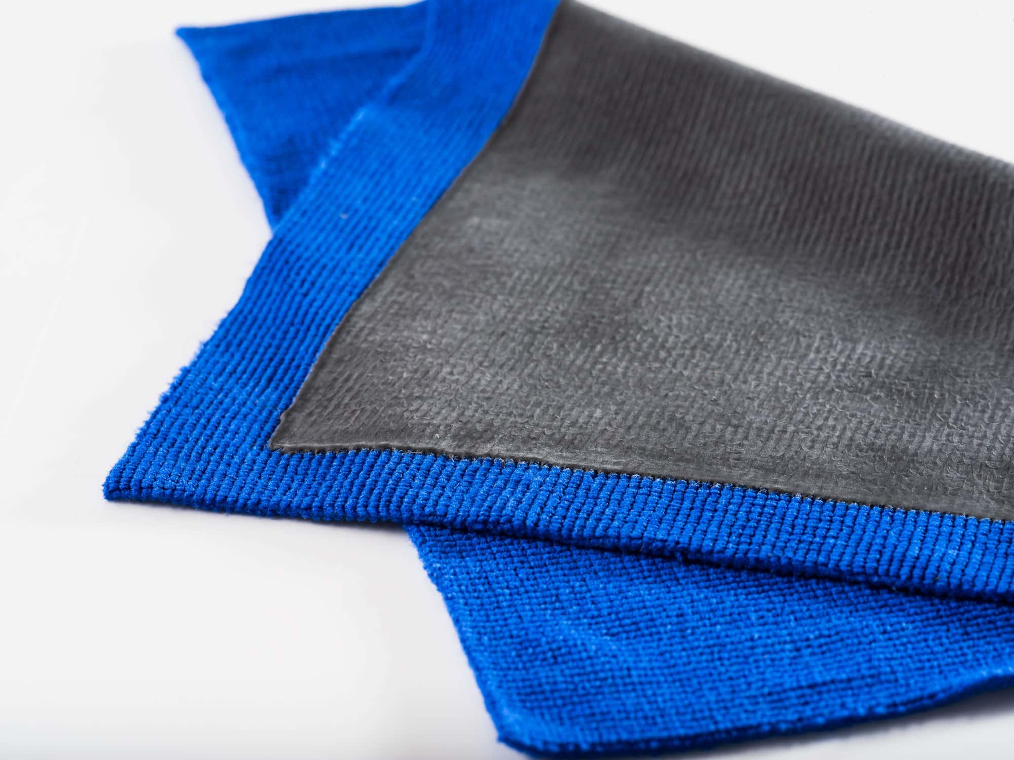 Blaues Mikrofasertuch mit schwarzer Unterseite, gerollt auf weißem Hintergrund für professionelle Reinigung