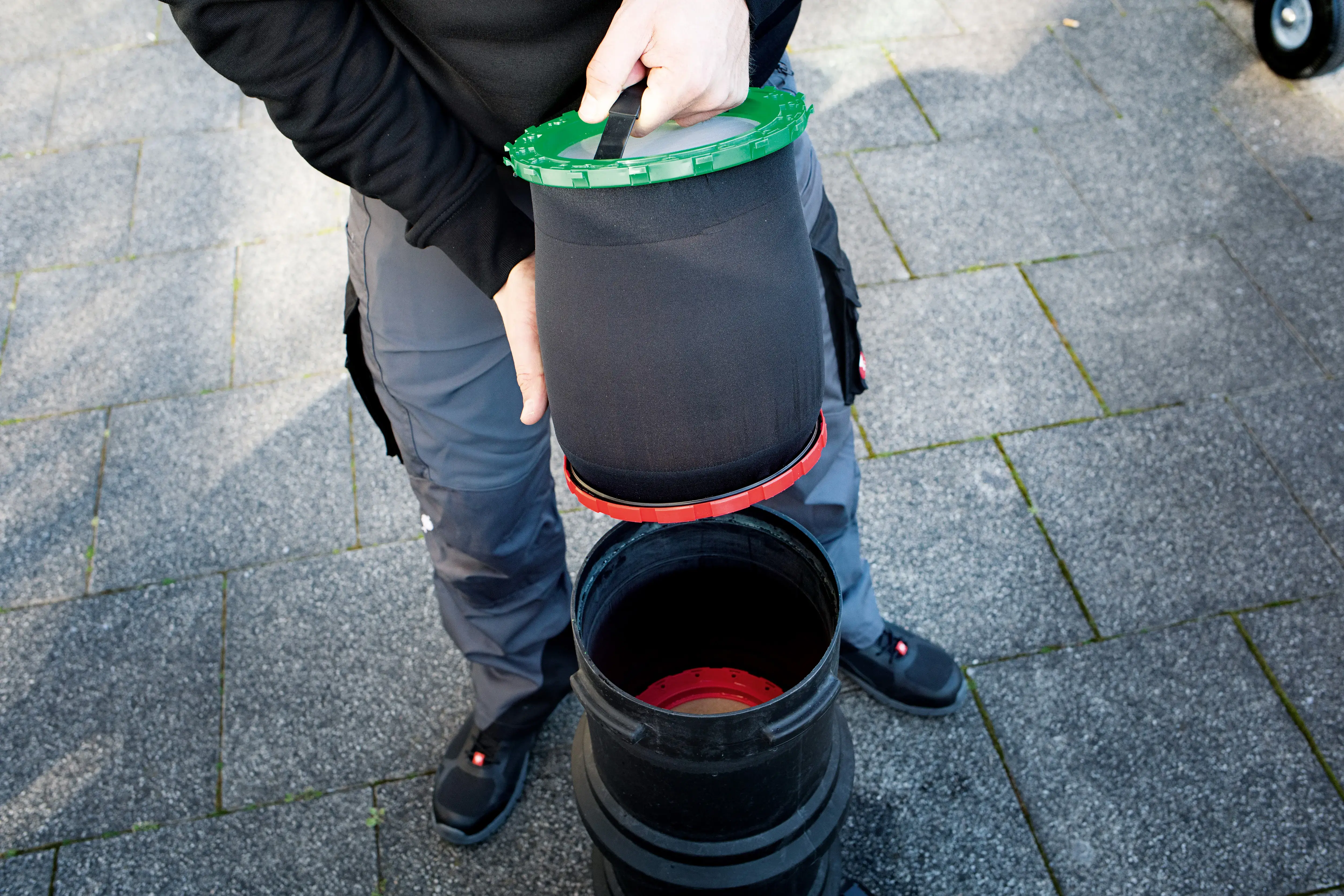 Person hält einen schwarzen Filter mit grünem Deckel über einem Behälter.