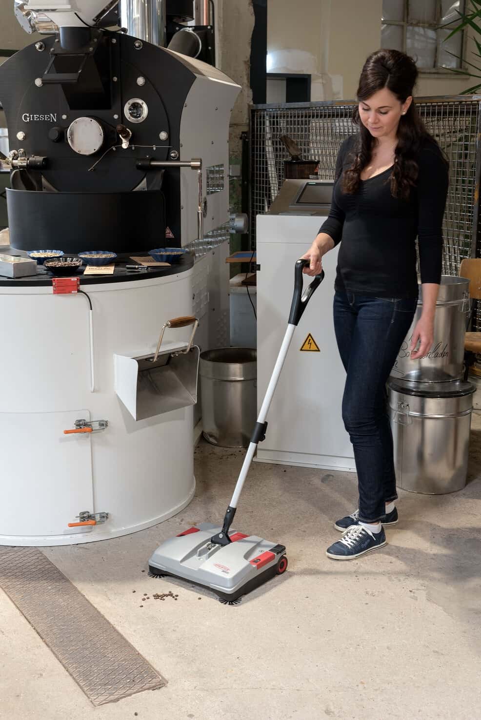 MEDUSA Akku-Kehrmaschine im Einsatz Frau benutzt die batteriebetriebene Kehrmaschine MEDUSA in einer Kaffeerösterei.